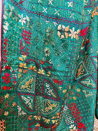 Close-up seated view of emerald green Lambani embroidered saree with red border