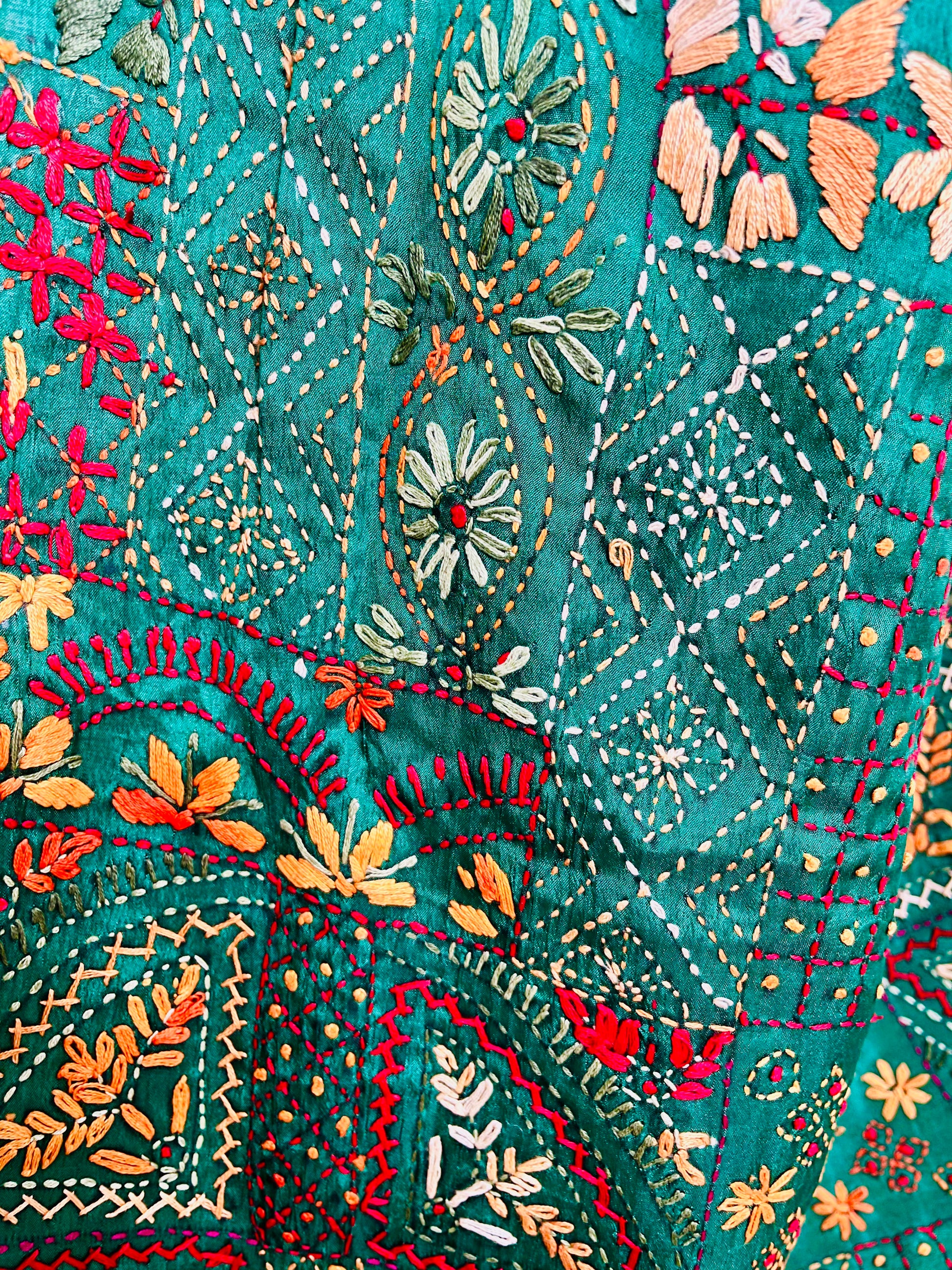 Close-up seated view of emerald green Lambani embroidered saree with red border