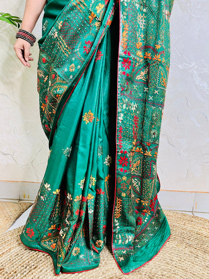 Close-up seated view of emerald green Lambani embroidered saree with red border