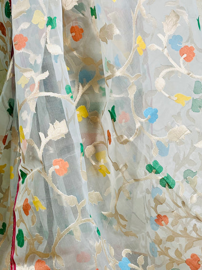 A close-up of a sheer white organza fabric with intricate gold floral embroidery and scattered colorful floral accents in orange, blue, green, and yellow.