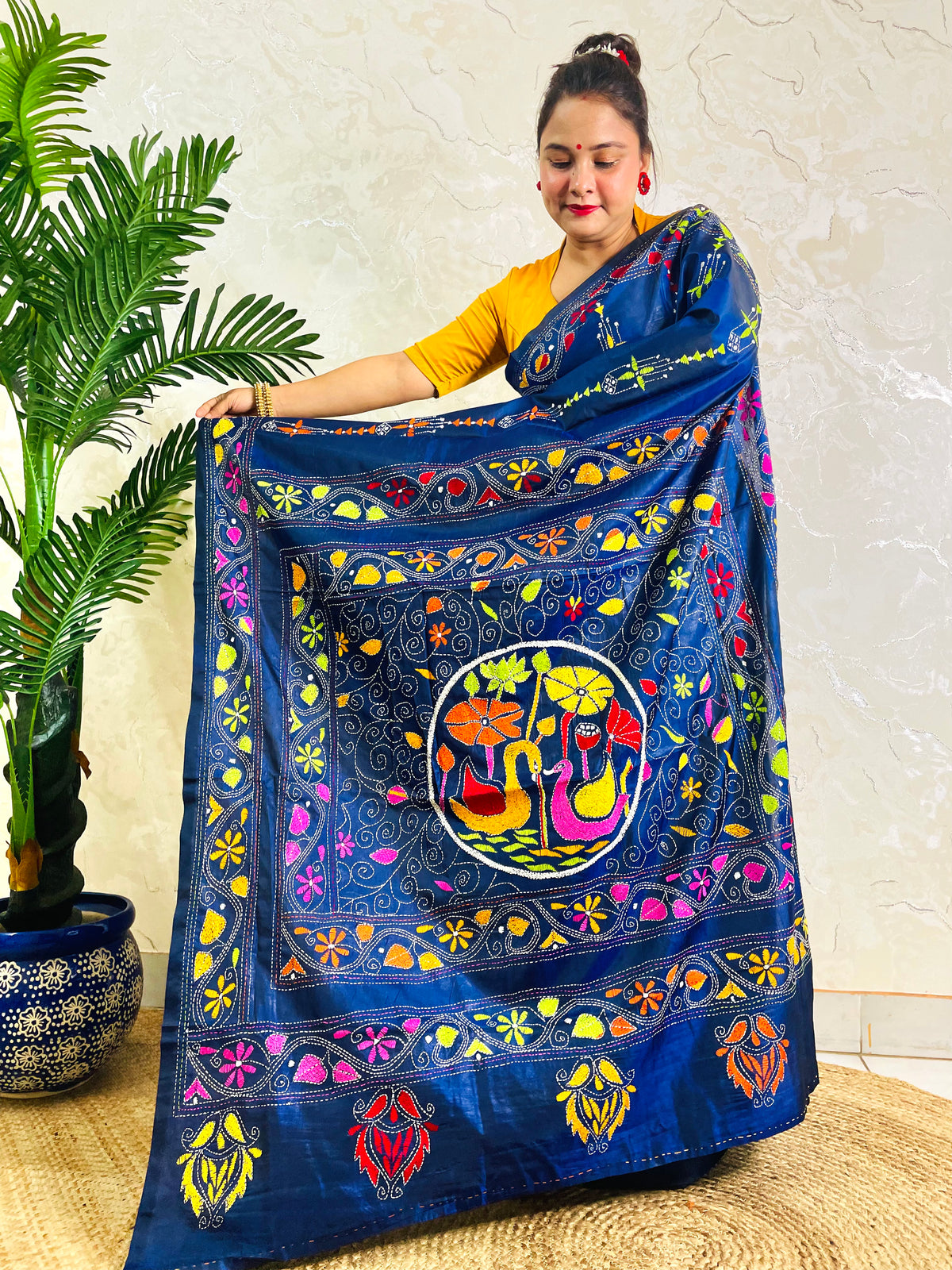 Woman holding open pallu of ink blue Kantha saree showing swan medallion