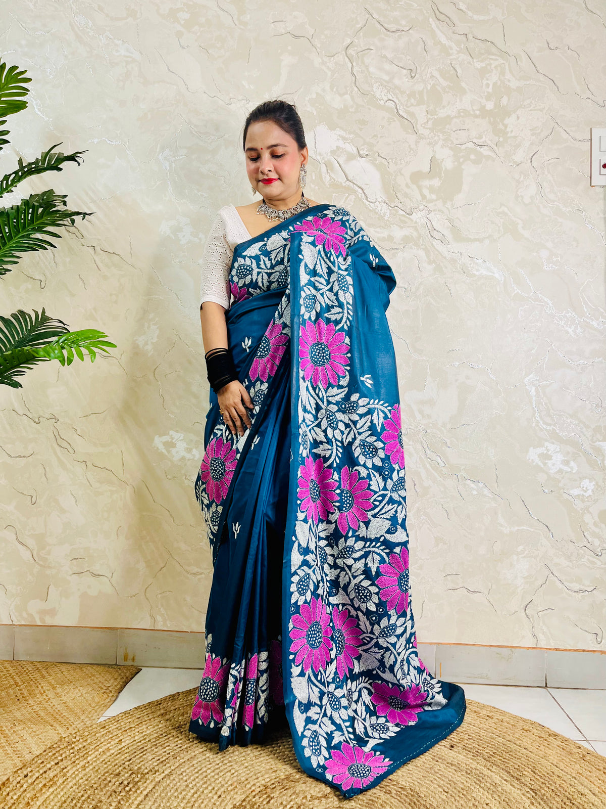 Pallu held open showing rows of magenta sunflowers and white leaf vines on peacock blue saree
