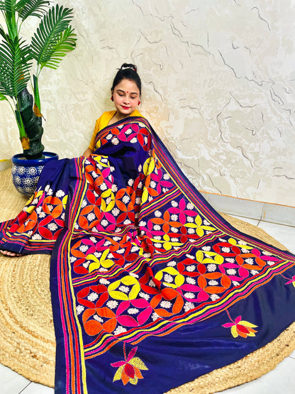 Woman seated in deep indigo Kantha saree with multicolour geometric border, side view