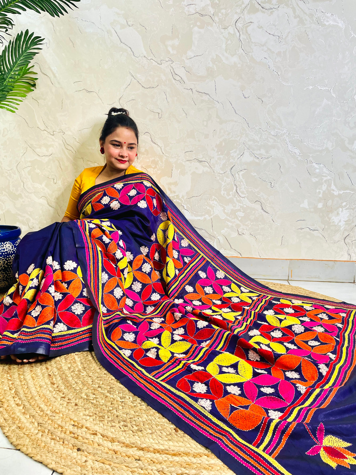 Woman seated in deep indigo Kantha saree with multicolour geometric border, side view