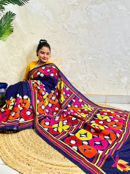 Woman seated in deep indigo Kantha saree with multicolour geometric border, side view