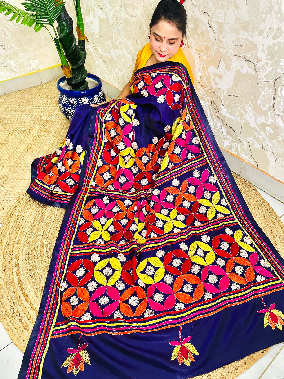 Woman seated in deep indigo Kantha saree with multicolour geometric border, side view