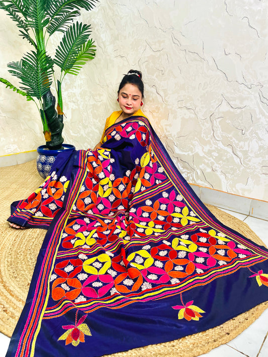 Woman seated in deep indigo Kantha saree with multicolour geometric border, side view