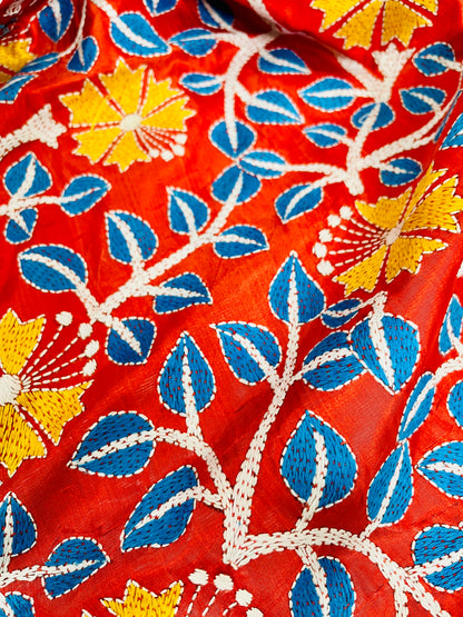 Detail of white and sky blue Kutch work cross-stitch lattice beside Kantha leaf motifs on vermilion silk