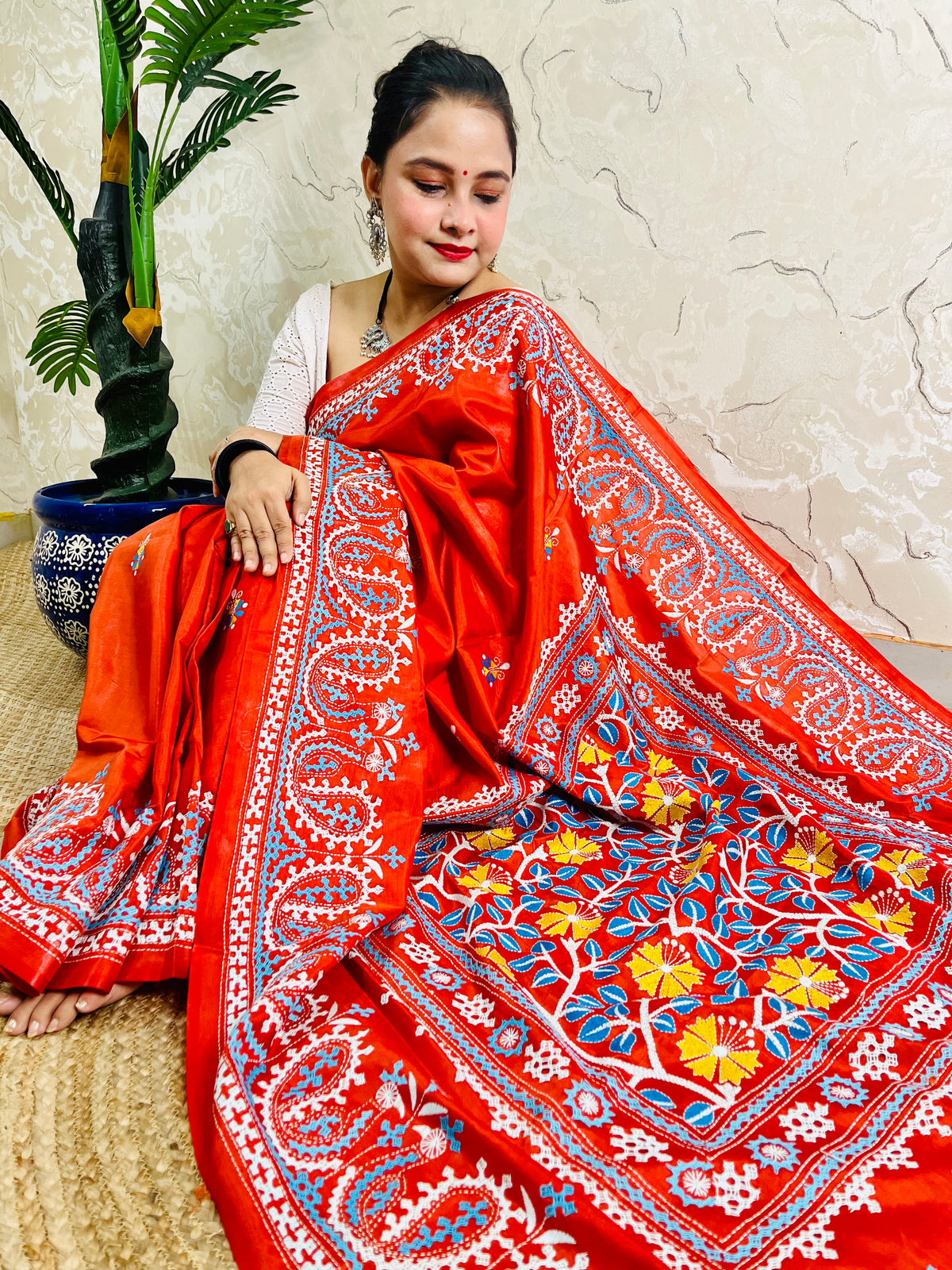 Seated pose in vermilion Kutch and Kantha fusion saree with paisley hem border