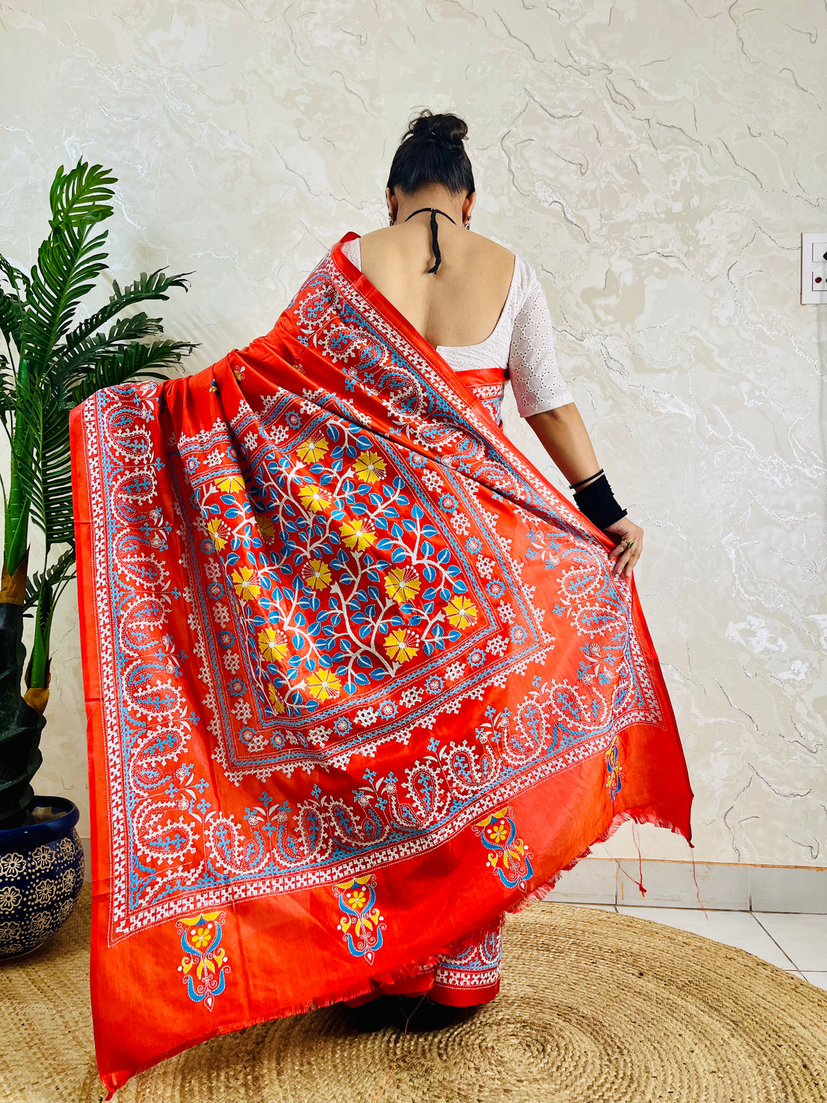Detail of white and sky blue Kutch work cross-stitch lattice beside Kantha leaf motifs on vermilion silk