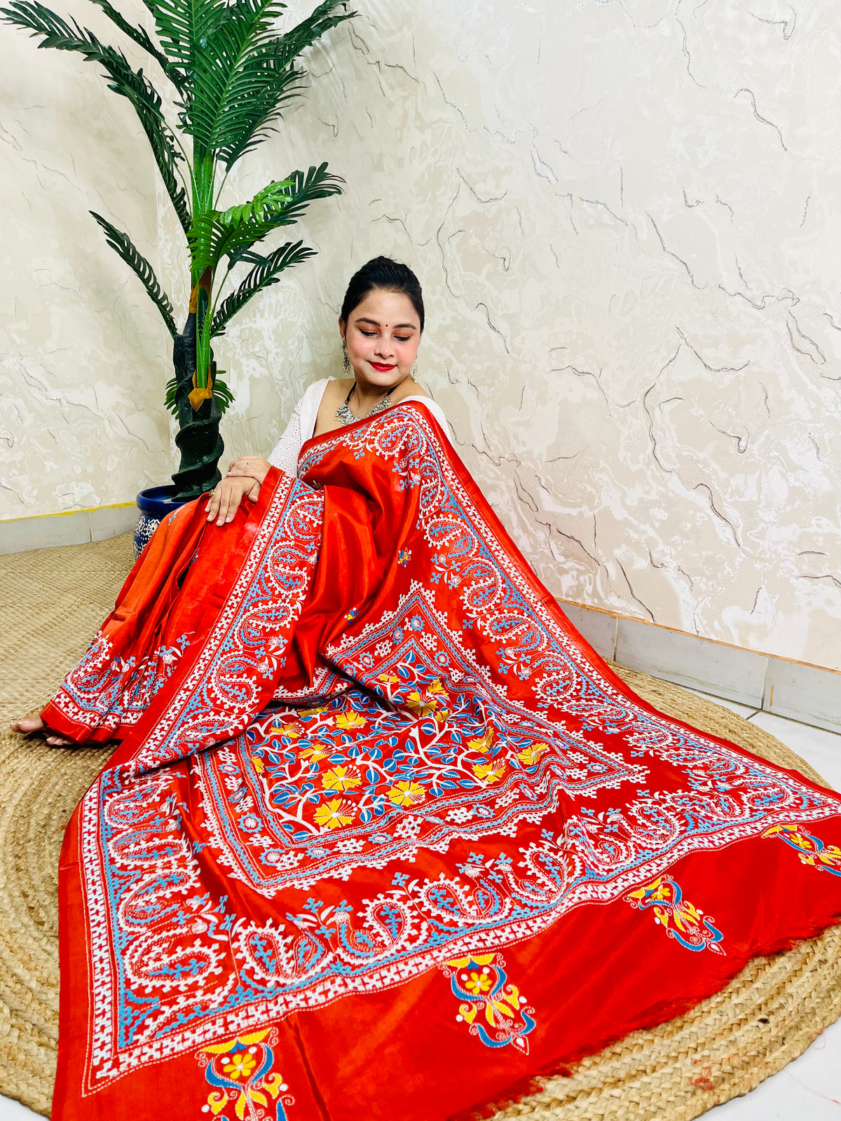 Seated pose in vermilion Kutch and Kantha fusion saree with paisley hem border