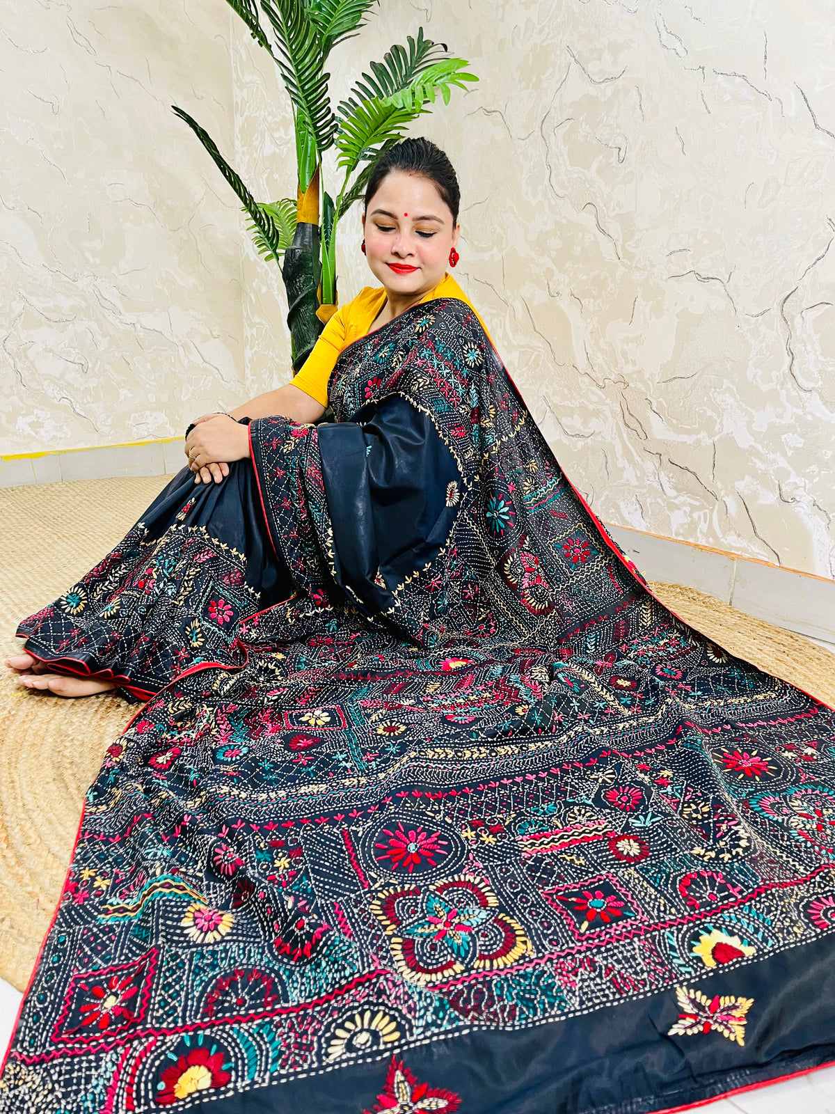 Woman seated in black Bangalore silk saree with Lambani thread embroidery