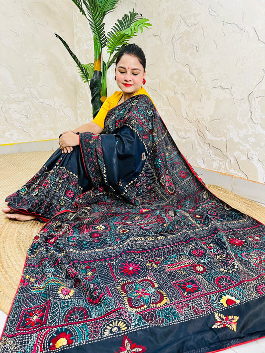 Woman seated in black Bangalore silk saree with Lambani thread embroidery