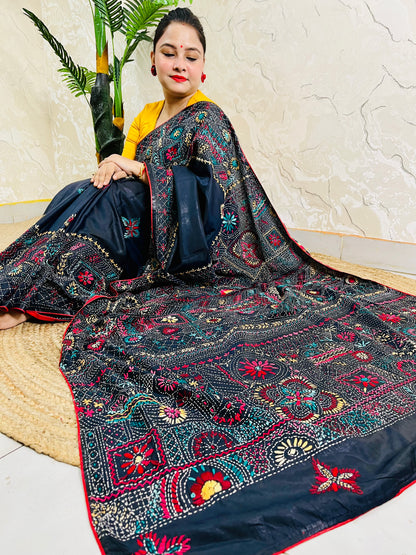 Woman seated in black Bangalore silk saree with Lambani thread embroidery