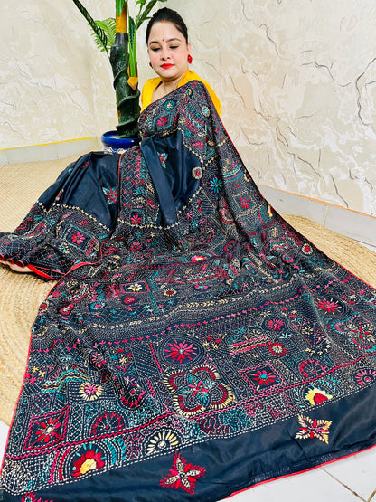Woman seated in black Bangalore silk saree with Lambani thread embroidery