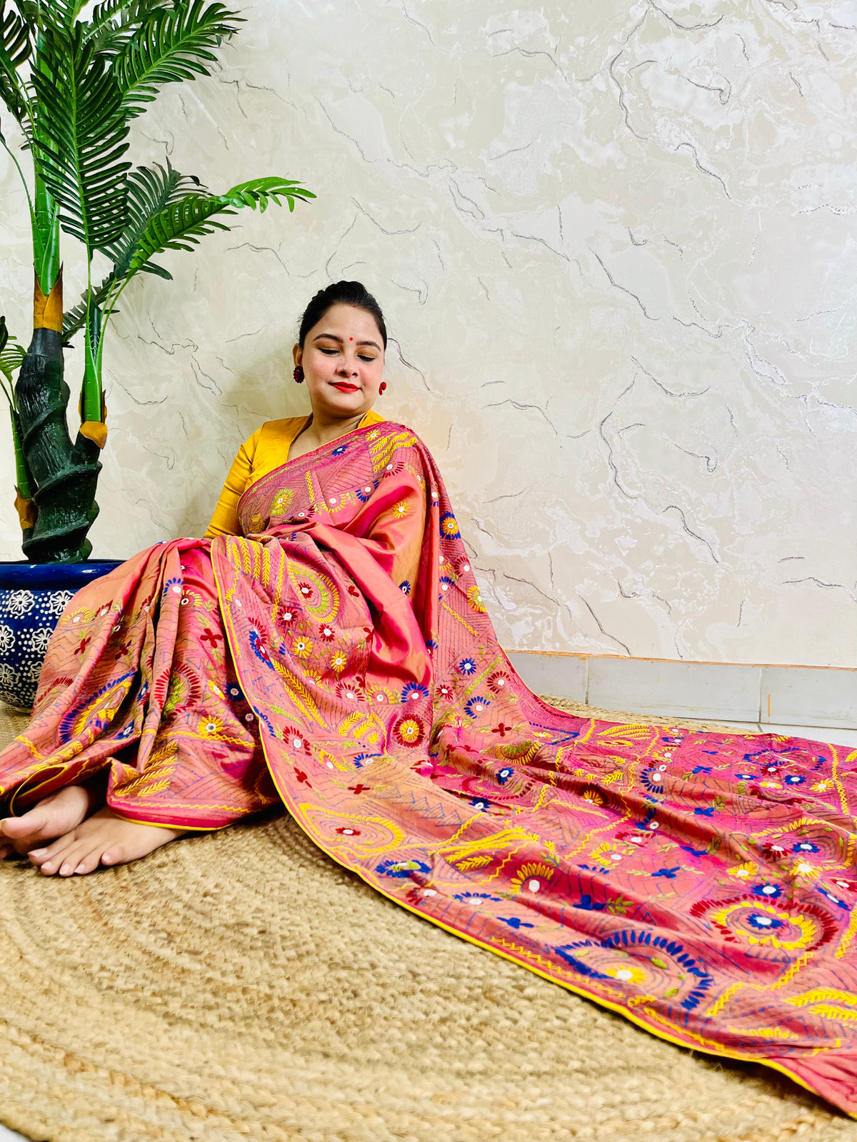 Woman seated in coral pink Lambani embroidered saree, draped pallu view