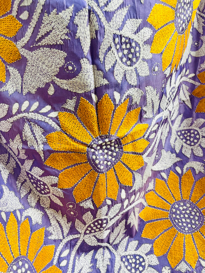 Macro texture close-up of the fine Katha stitch running embroidery outlining the bright yellow sunflower petals and white foliage.