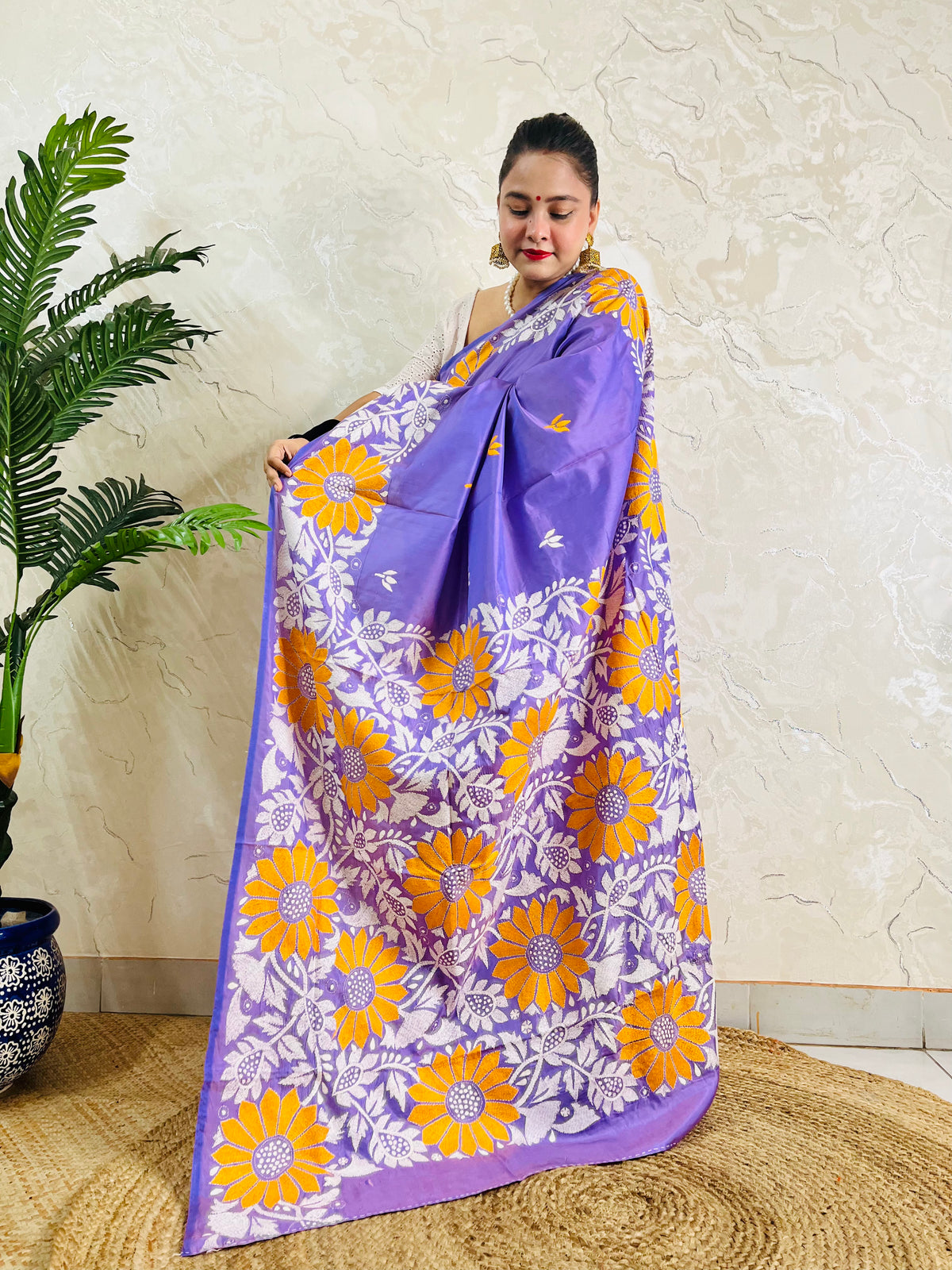 Full front display of a woman holding up the lavender violet silk saree, revealing the dense yellow sunflower and white vine Kantha embroidery on the pallu