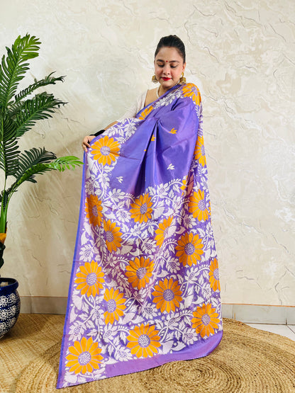 Full front display of a woman holding up the lavender violet silk saree, revealing the dense yellow sunflower and white vine Kantha embroidery on the pallu