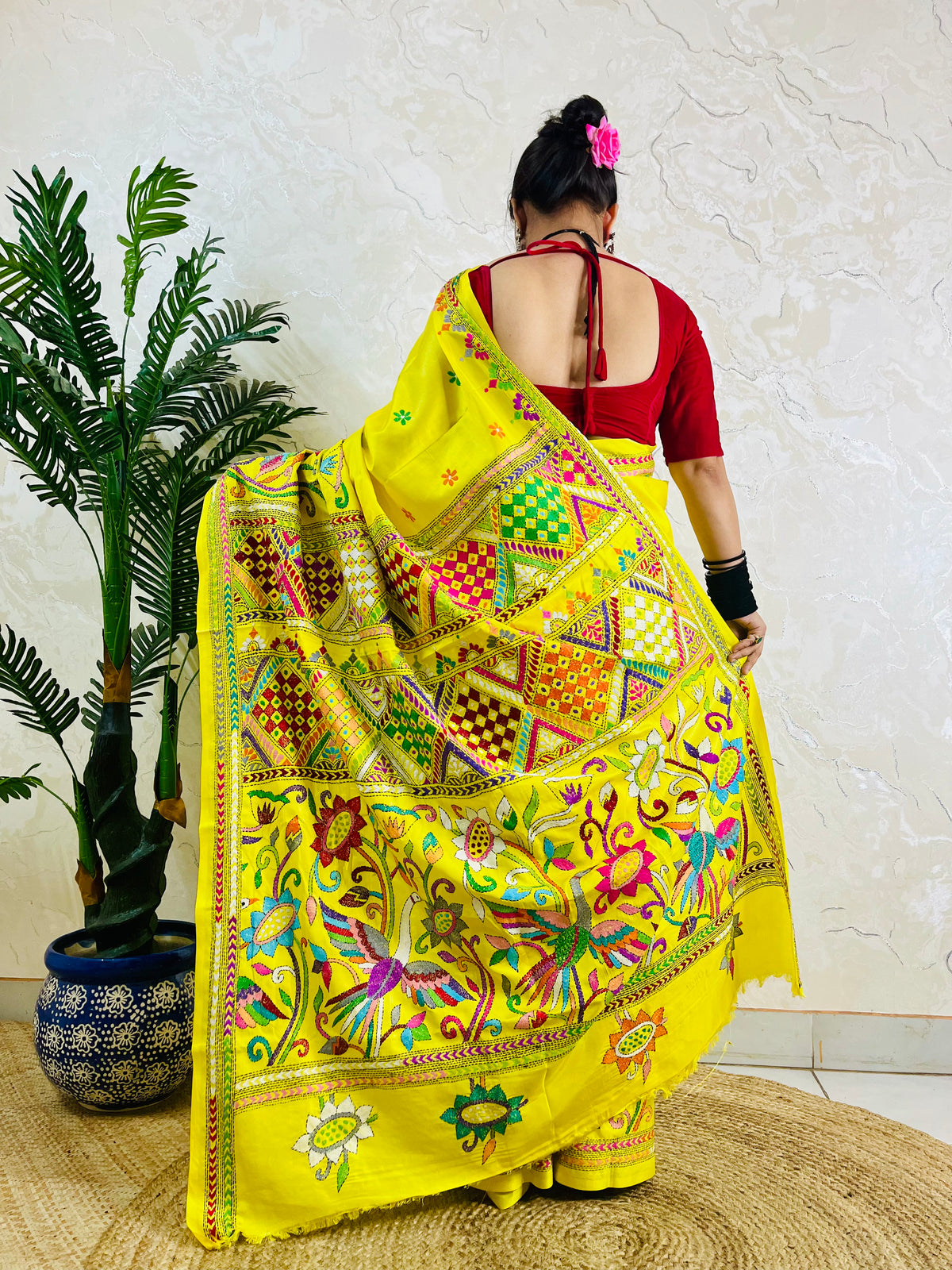 Back view of a woman wearing the handcrafted yellow Bangalore silk saree, emphasizing the striking placement of the bird and floral Nakshi Kantha stitch work on the flowing pallu