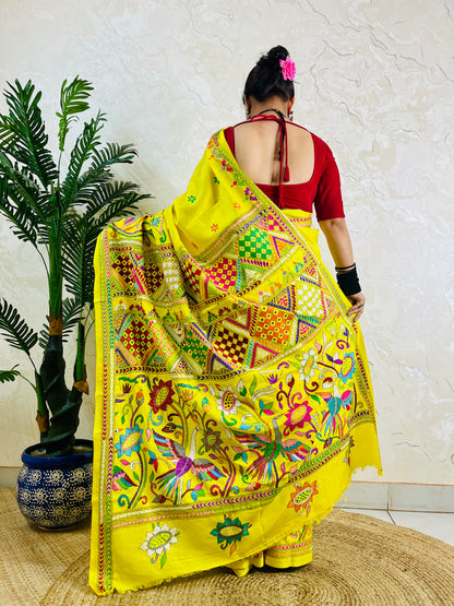 Back view of a woman wearing the handcrafted yellow Bangalore silk saree, emphasizing the striking placement of the bird and floral Nakshi Kantha stitch work on the flowing pallu