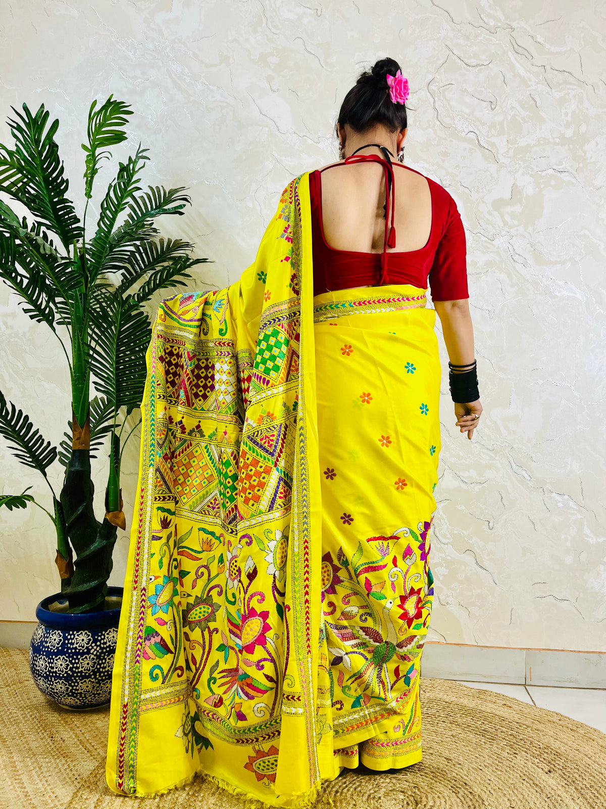 Back view of a woman wearing the handcrafted yellow Bangalore silk saree, emphasizing the striking placement of the bird and floral Nakshi Kantha stitch work on the flowing pallu