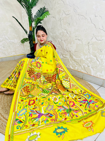 Woman sitting gracefully while draped in the vibrant sunny yellow Nakshi Katha saree, showcasing the densely embroidered, multi-colored border and pallu
