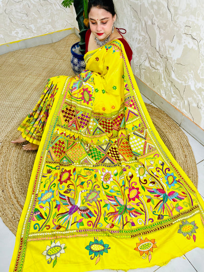 Woman sitting gracefully while draped in the vibrant sunny yellow Nakshi Katha saree, showcasing the densely embroidered, multi-colored border and pallu