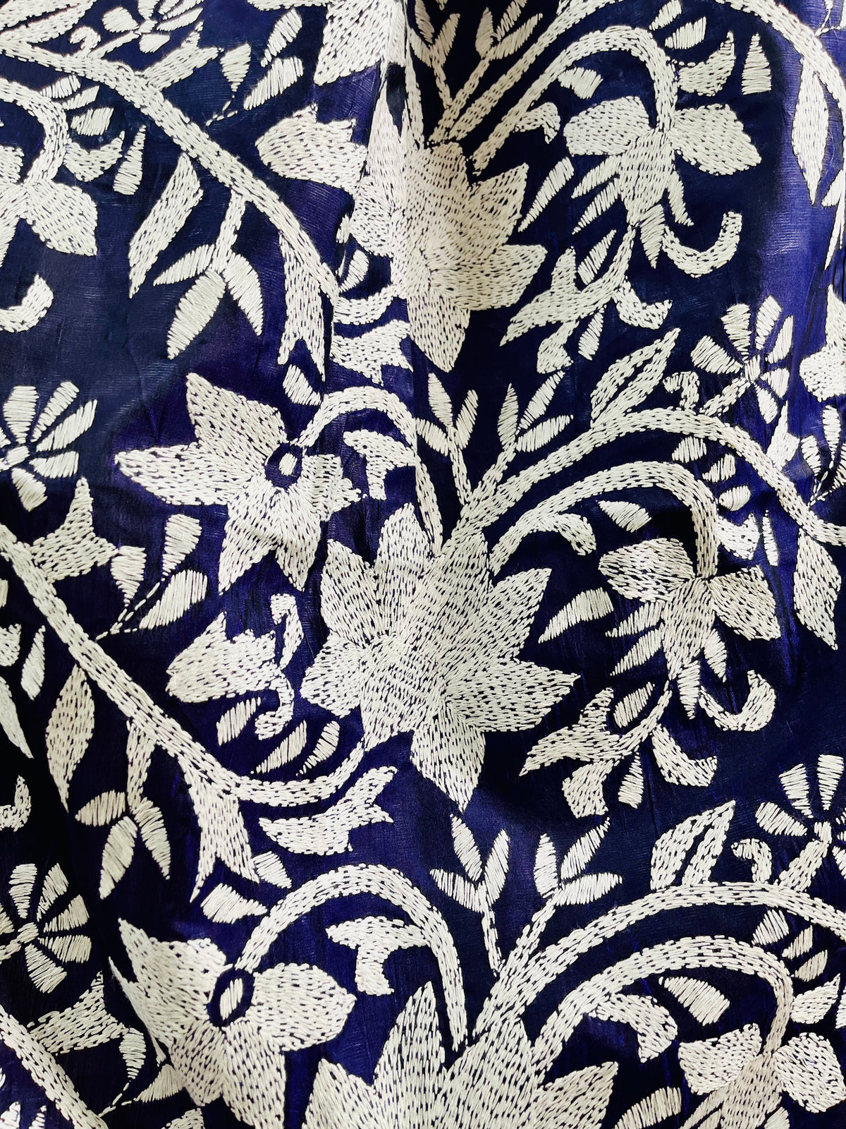 Close-up texture shot of the intricate hand-embroidered white thread Katha stitch flowers and flowing vines on deep navy silk.