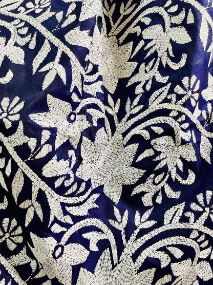 Close-up texture shot of the intricate hand-embroidered white thread Katha stitch flowers and flowing vines on deep navy silk.
