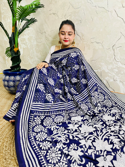 Woman sitting draped in the navy blue Kantha silk saree, spreading out the dense white floral vine embroidery on the pallu.