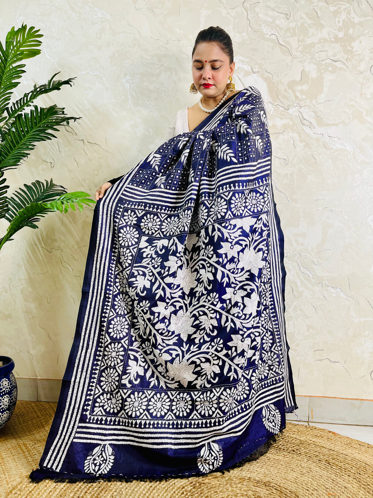 Woman holding up the magnificent pallu of the navy blue Katha saree to highlight the intricate floral mandala and vine artwork.