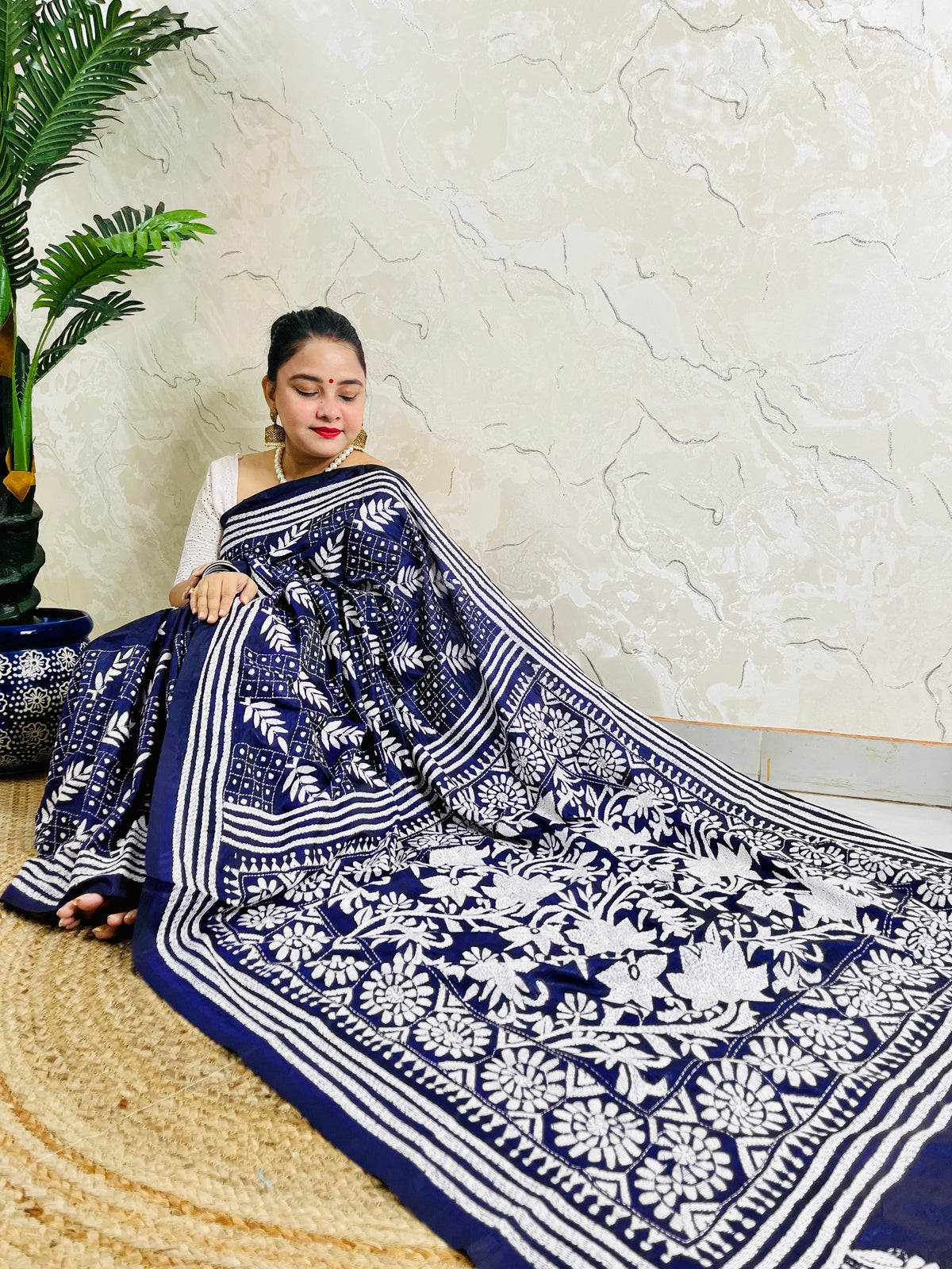 Woman sitting draped in the navy blue Kantha silk saree, spreading out the dense white floral vine embroidery on the pallu.