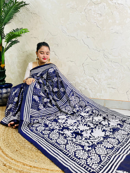 Woman sitting draped in the navy blue Kantha silk saree, spreading out the dense white floral vine embroidery on the pallu.