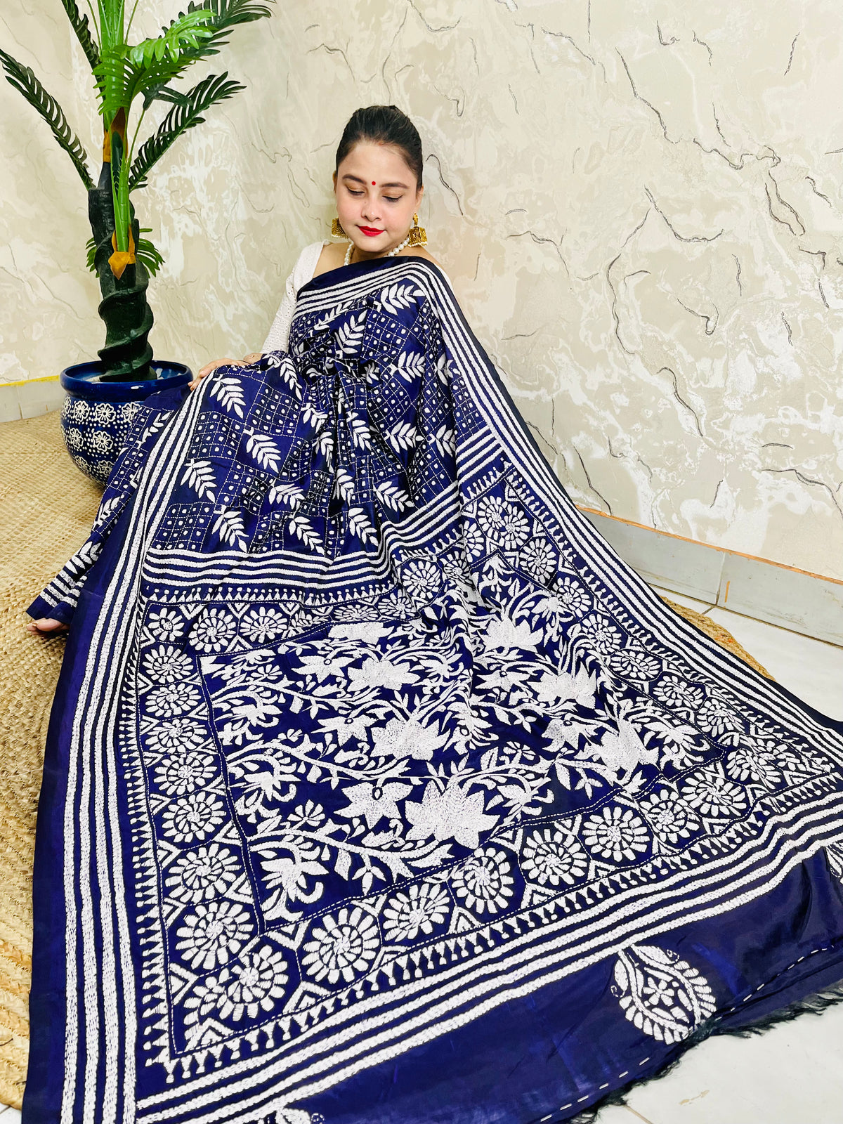 Woman sitting draped in the navy blue Kantha silk saree, spreading out the dense white floral vine embroidery on the pallu.