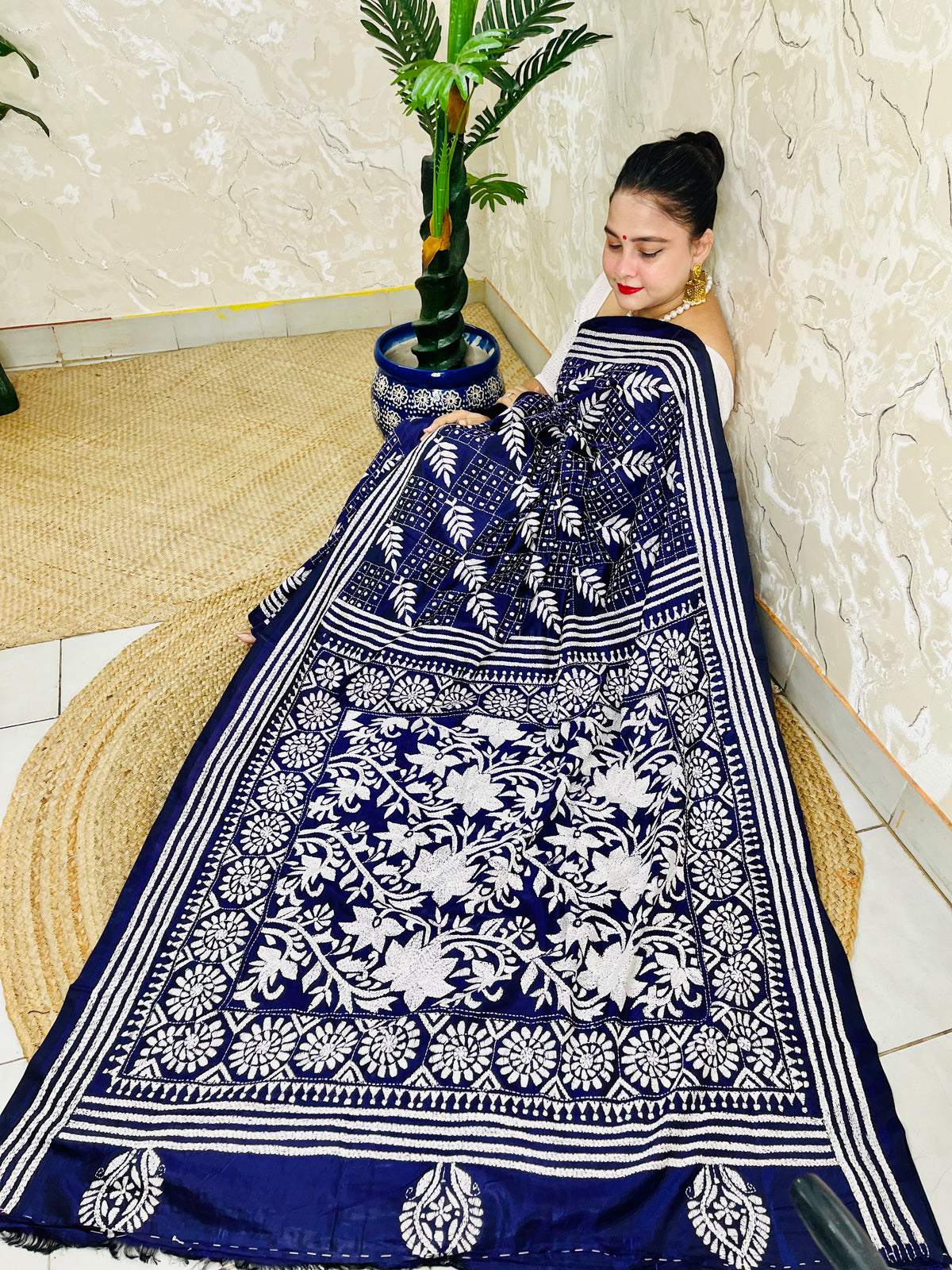Woman sitting draped in the navy blue Kantha silk saree, spreading out the dense white floral vine embroidery on the pallu.