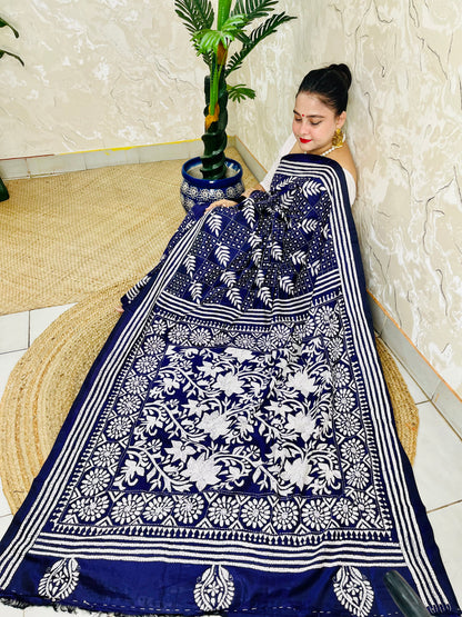 Woman sitting draped in the navy blue Kantha silk saree, spreading out the dense white floral vine embroidery on the pallu.