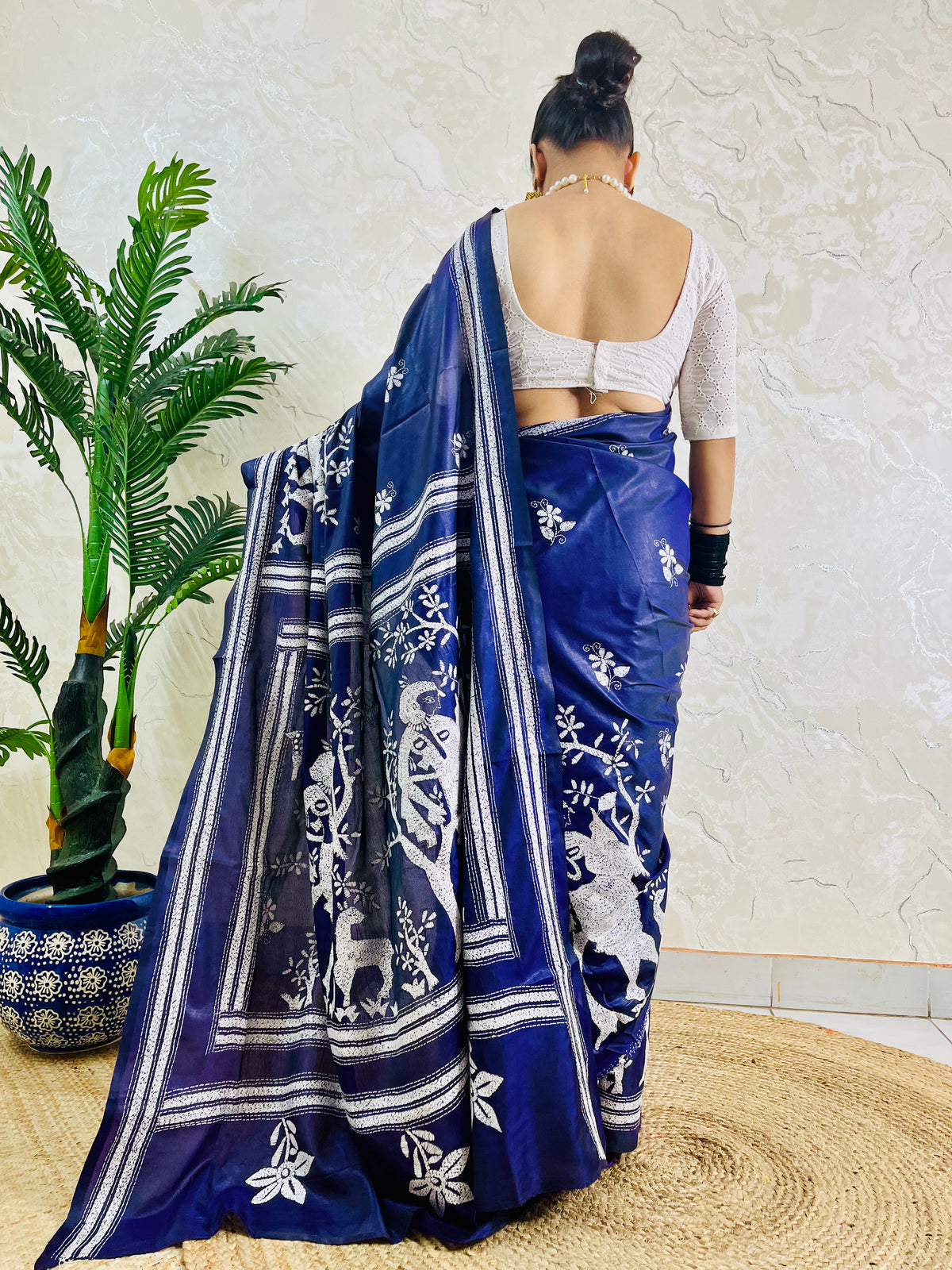 Rear view of woman draped in the navy blue handcrafted saree, highlighting the expansive village tapestry embroidered on the pallu.
