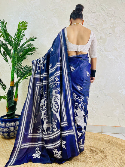 Rear view of woman draped in the navy blue handcrafted saree, highlighting the expansive village tapestry embroidered on the pallu.