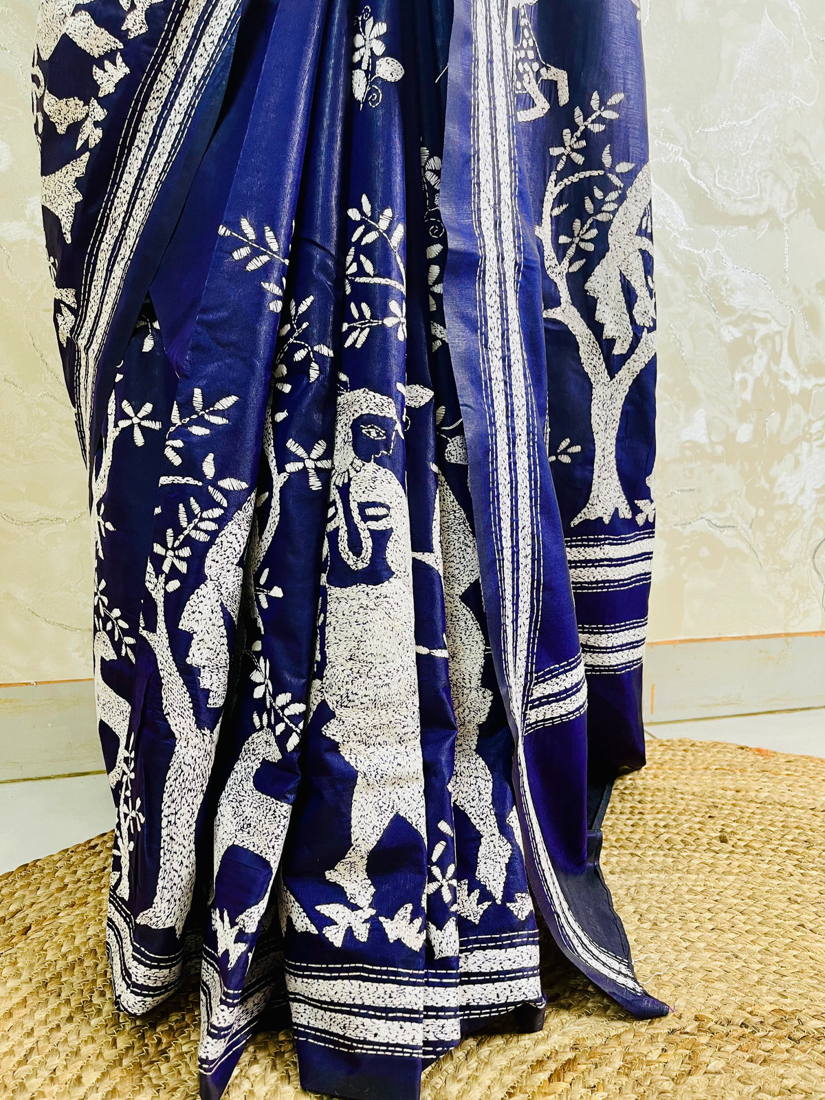 Close-up shot of white running thread Katha stitch embroidery depicting a Santhal flute player, trees, and deer on navy silk.