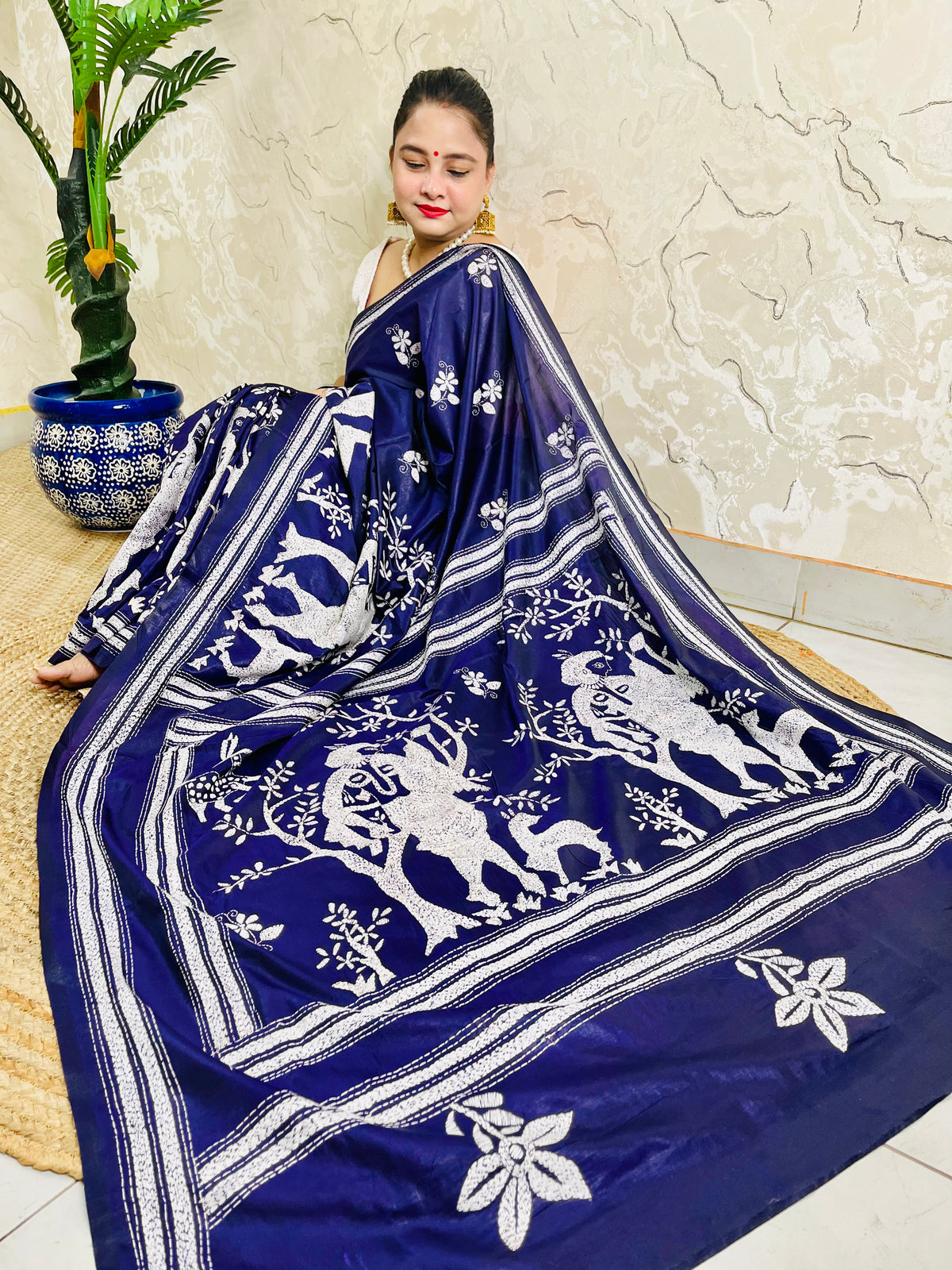 High-angle sitting pose showcasing the spread-out Santhal flute player and deer motif pallu embroidery on navy Bangalore silk.