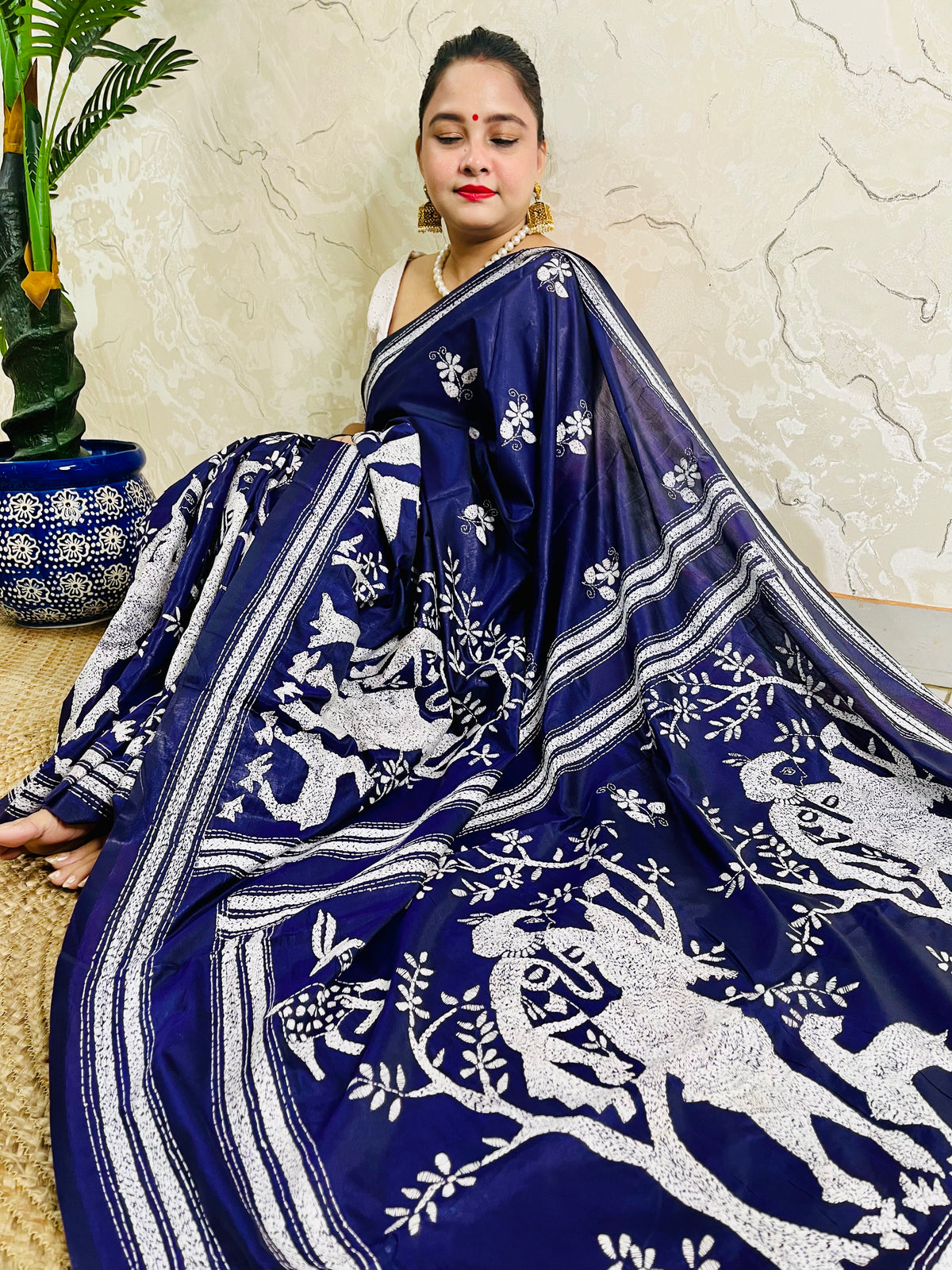 High-angle sitting pose showcasing the spread-out Santhal flute player and deer motif pallu embroidery on navy Bangalore silk.