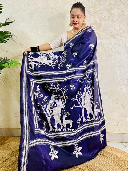 Model holding out the pallu of the navy blue Kantha silk saree to show the detailed tribal flute players standing under blooming trees.