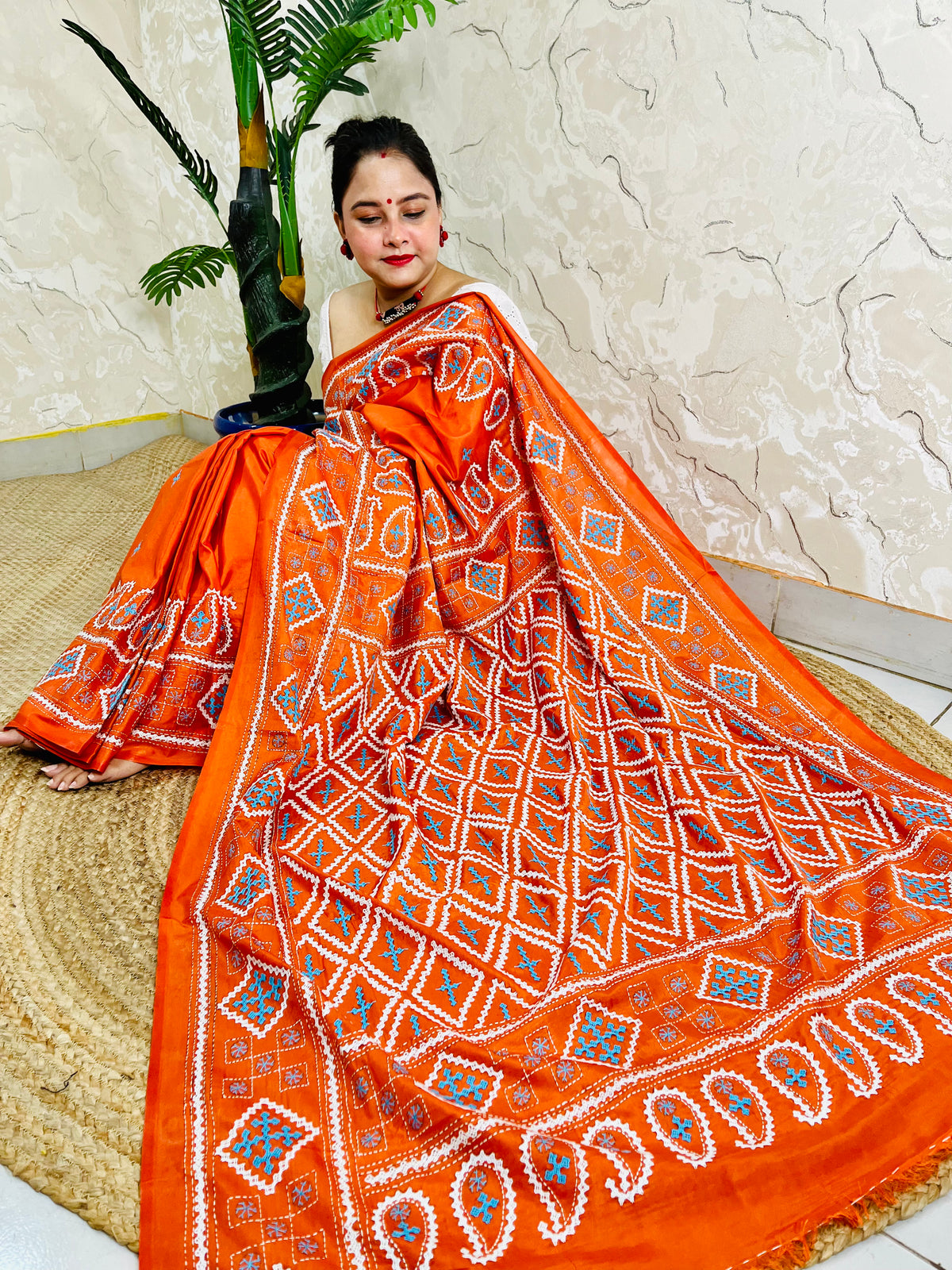 Seated pose showing orange saree pallu with Gujarati stitch geometric pattern