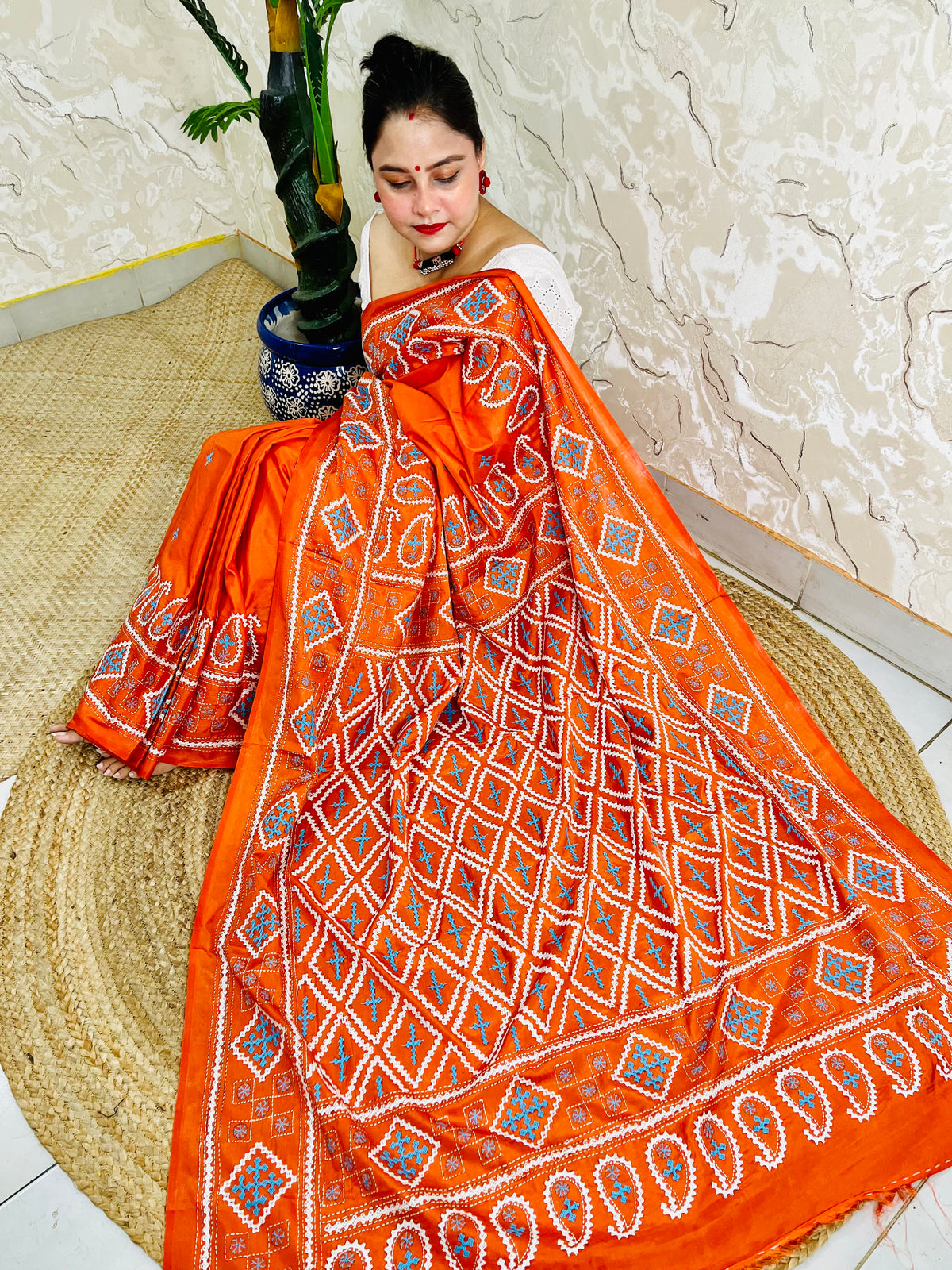 Seated pose showing orange saree pallu with Gujarati stitch geometric pattern