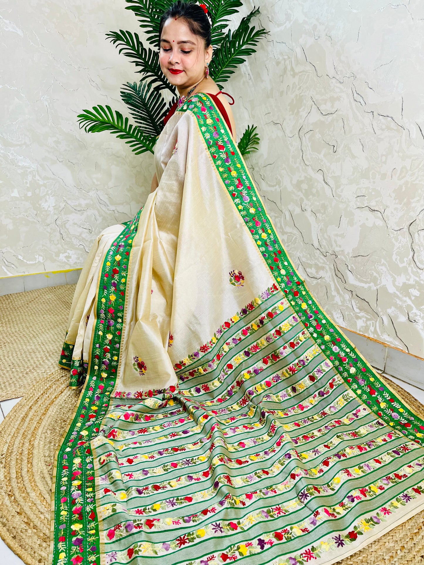 Side sitting view of Parsi Gara handwoven ivory Semi Muga Silk saree with emerald green velvet border and full multicolour floral garden pallu with woven stripe body — Desi Aadat