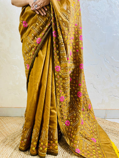 Close-up of all-over Jali trellis grid with pink daisy florals, yellow star stitches, and cream leaf Parsi Gara hand embroidery on golden brown Chanderi silk cotton saree — Desi Aadat