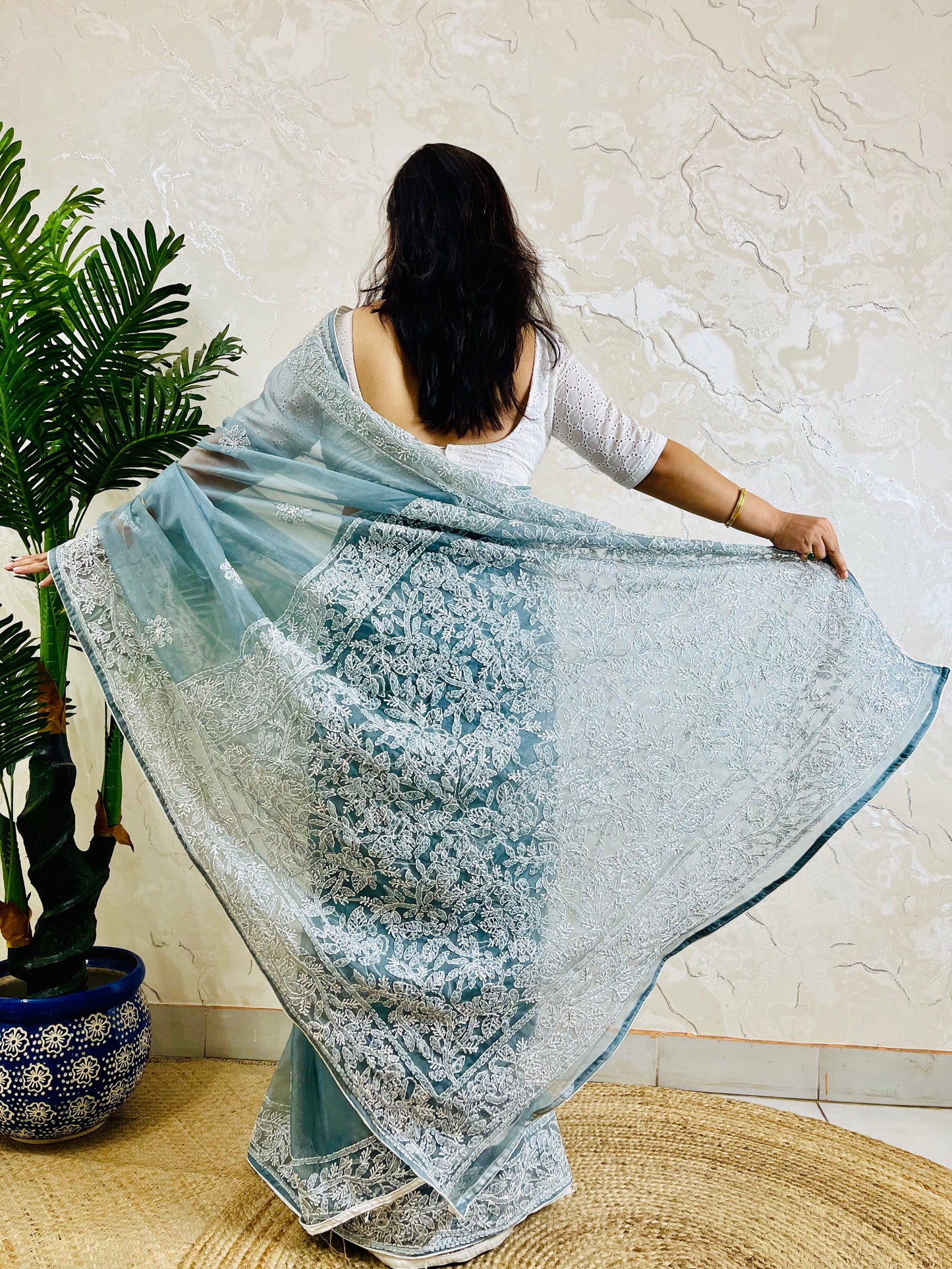 Pastel dusty blue Chikankari handstitched organza silk saree with structured white jaal embroidery — standing front view, Desi Aadat