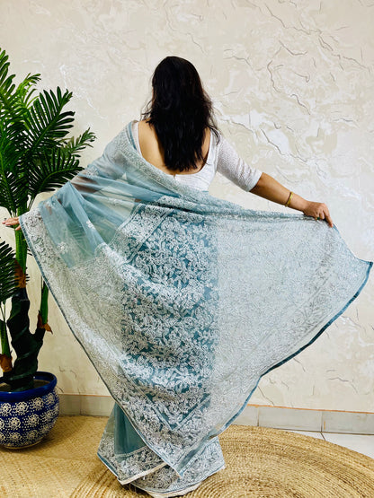 Pastel dusty blue Chikankari handstitched organza silk saree with structured white jaal embroidery — standing front view, Desi Aadat