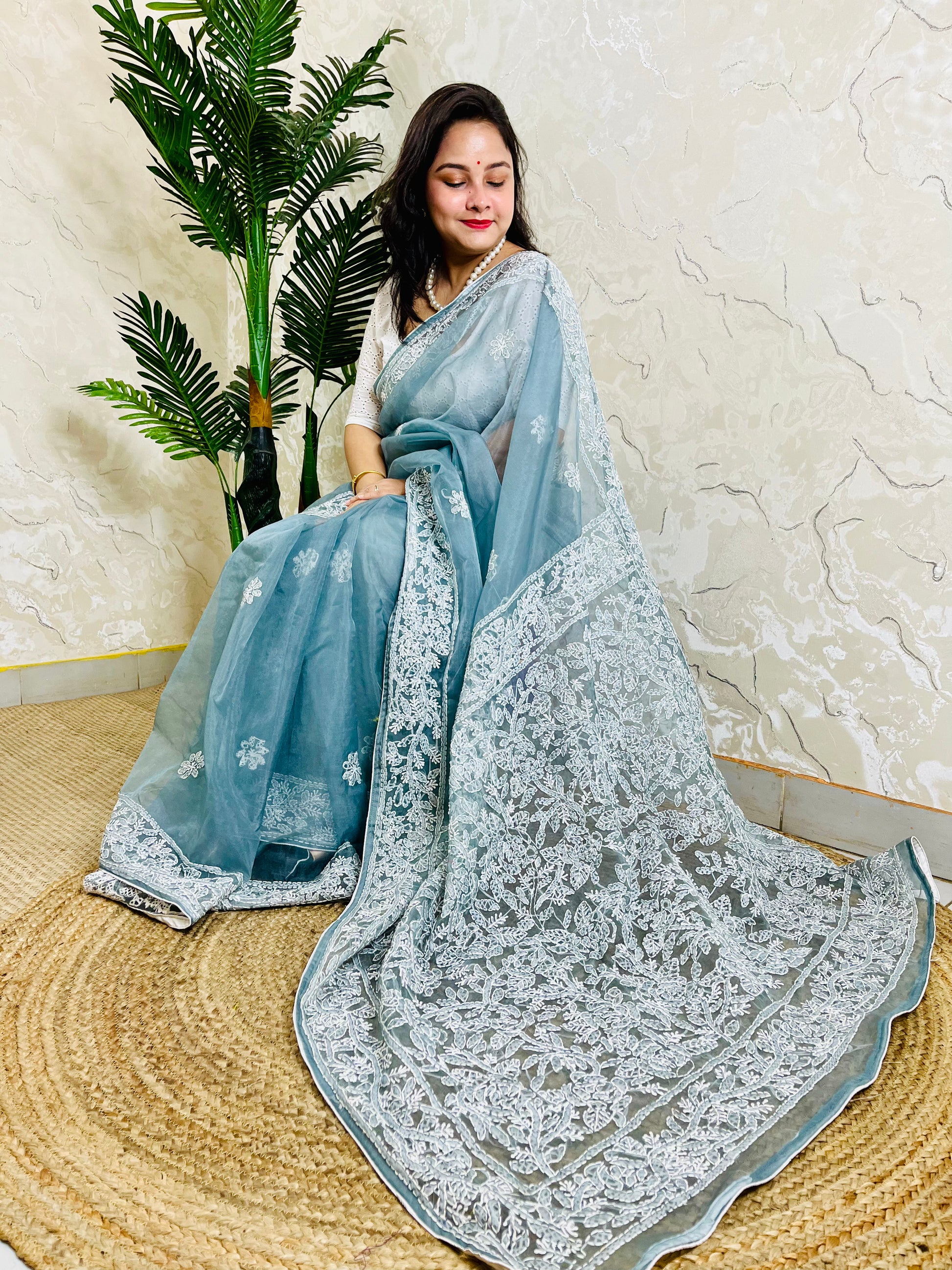 Handmade Lucknowi Chikankari pastel dusty blue pure organza silk saree with dense white jaal and floral embroidery — sitting drape view, Desi Aadat